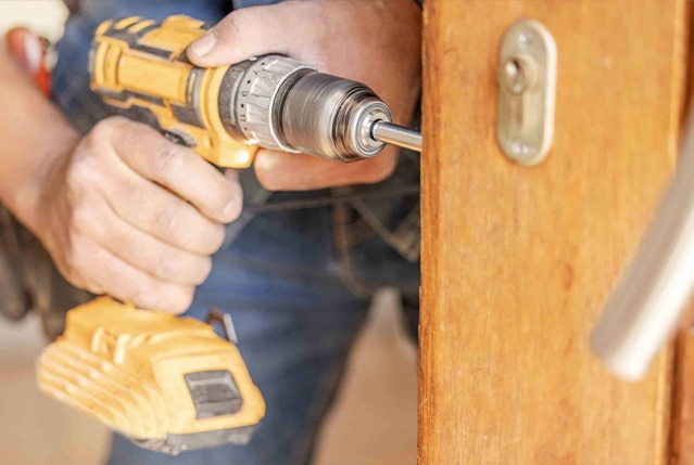 A handyman drilling into a door lock